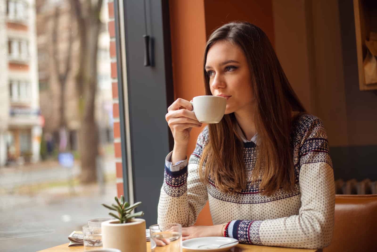 une belle femme aux longs cheveux bruns est assise et boit du café