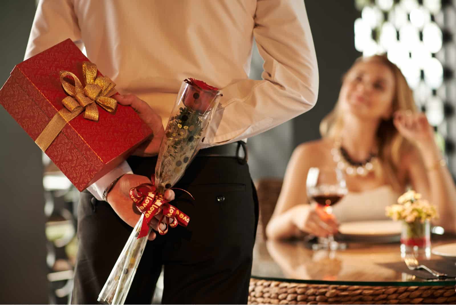 une femme assise à une table buvant du vin un homme tenant un cadeau