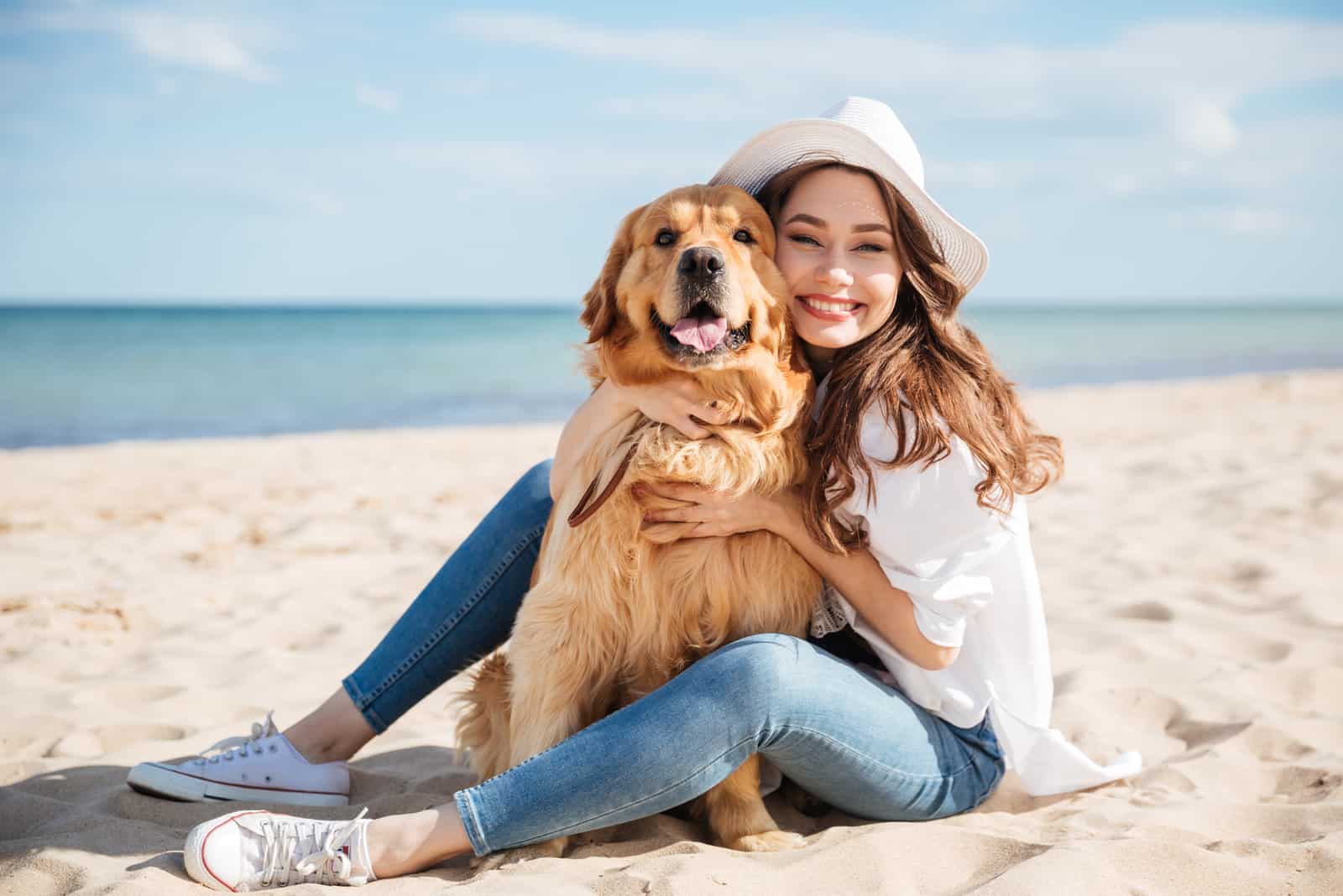 une femme souriante assise sur la plage serrant un chien