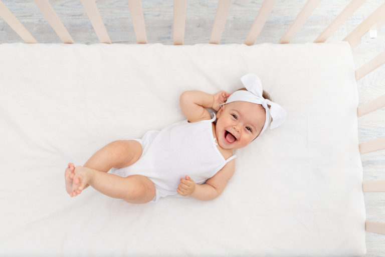 un bébé souriant avec une grosse tête se trouve dans un berceau
