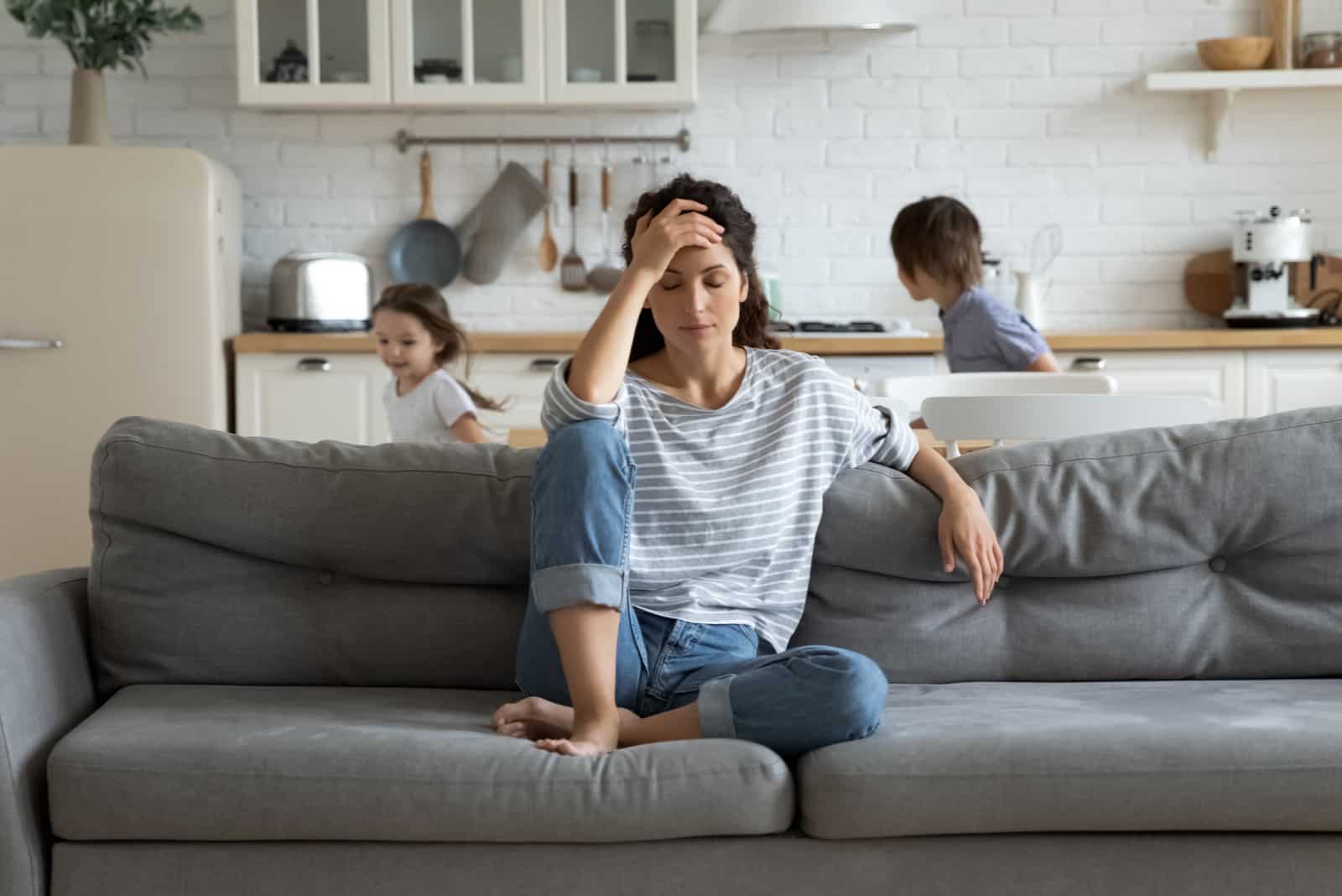 mère tenant sa tête pendant que les enfants courent en arrière-plan