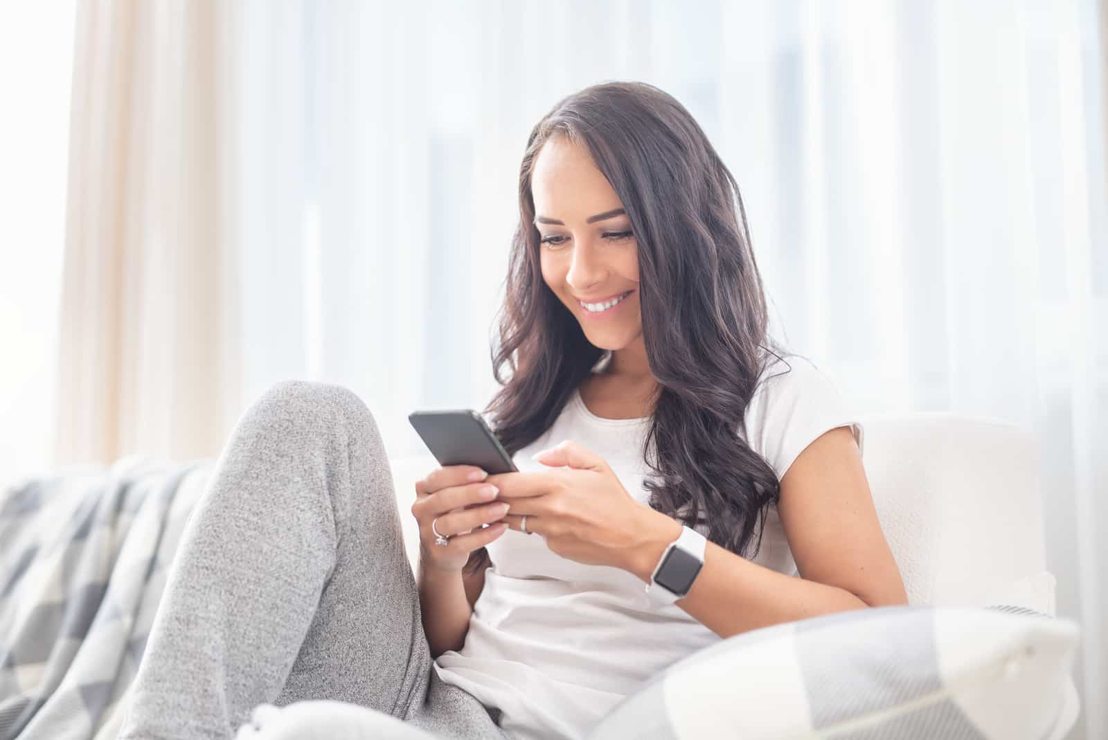 une femme souriante est assise sur le canapé et les touches du téléphone