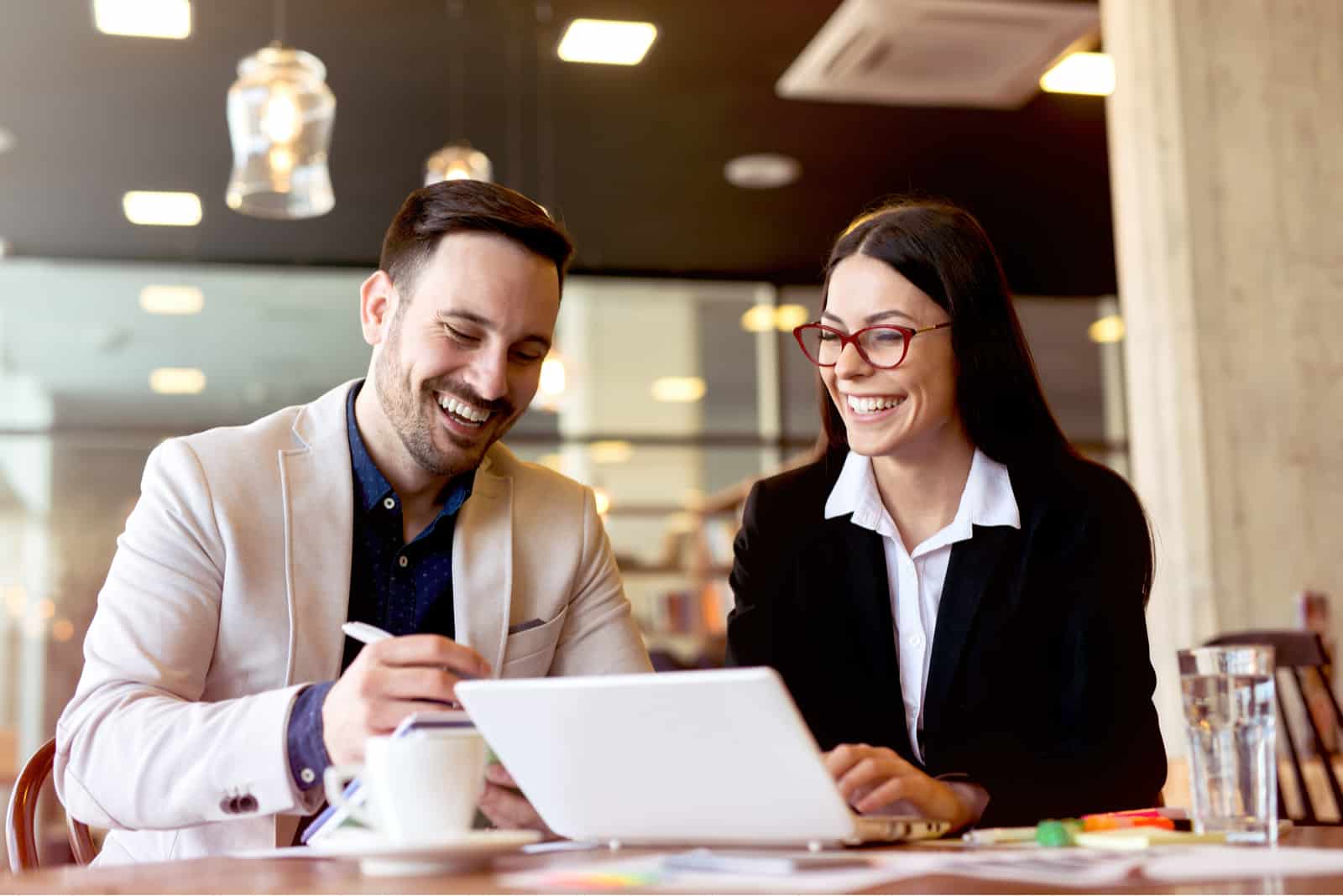 un homme et une femme souriants sont assis devant un ordinateur portable et parlent