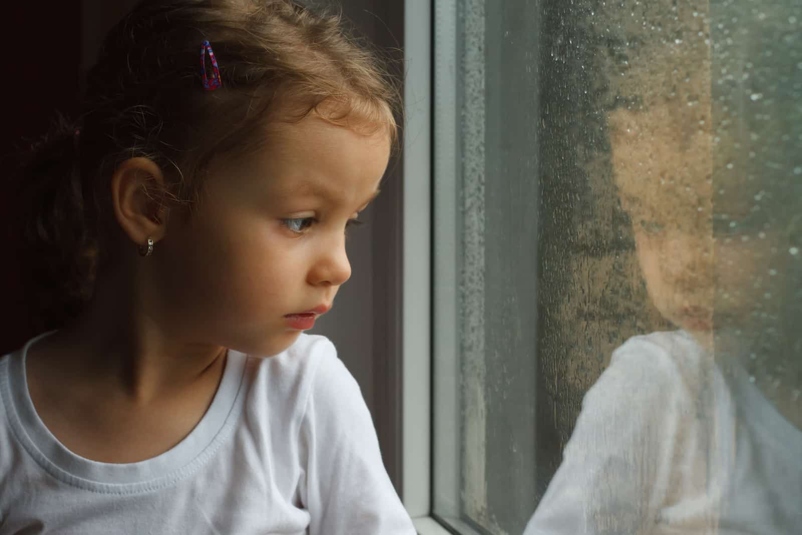 triste petite fille regardant par la fenêtre