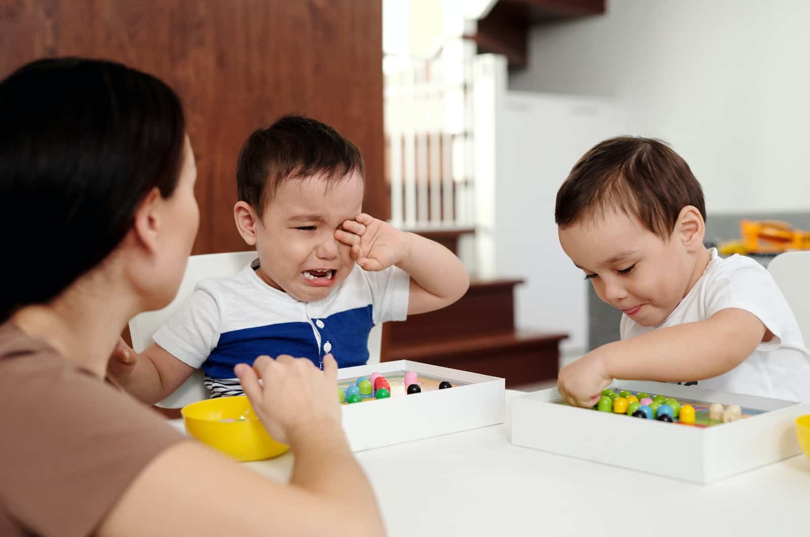 deux garçons et une mère jouant à des jeux pendant que l'un pleure