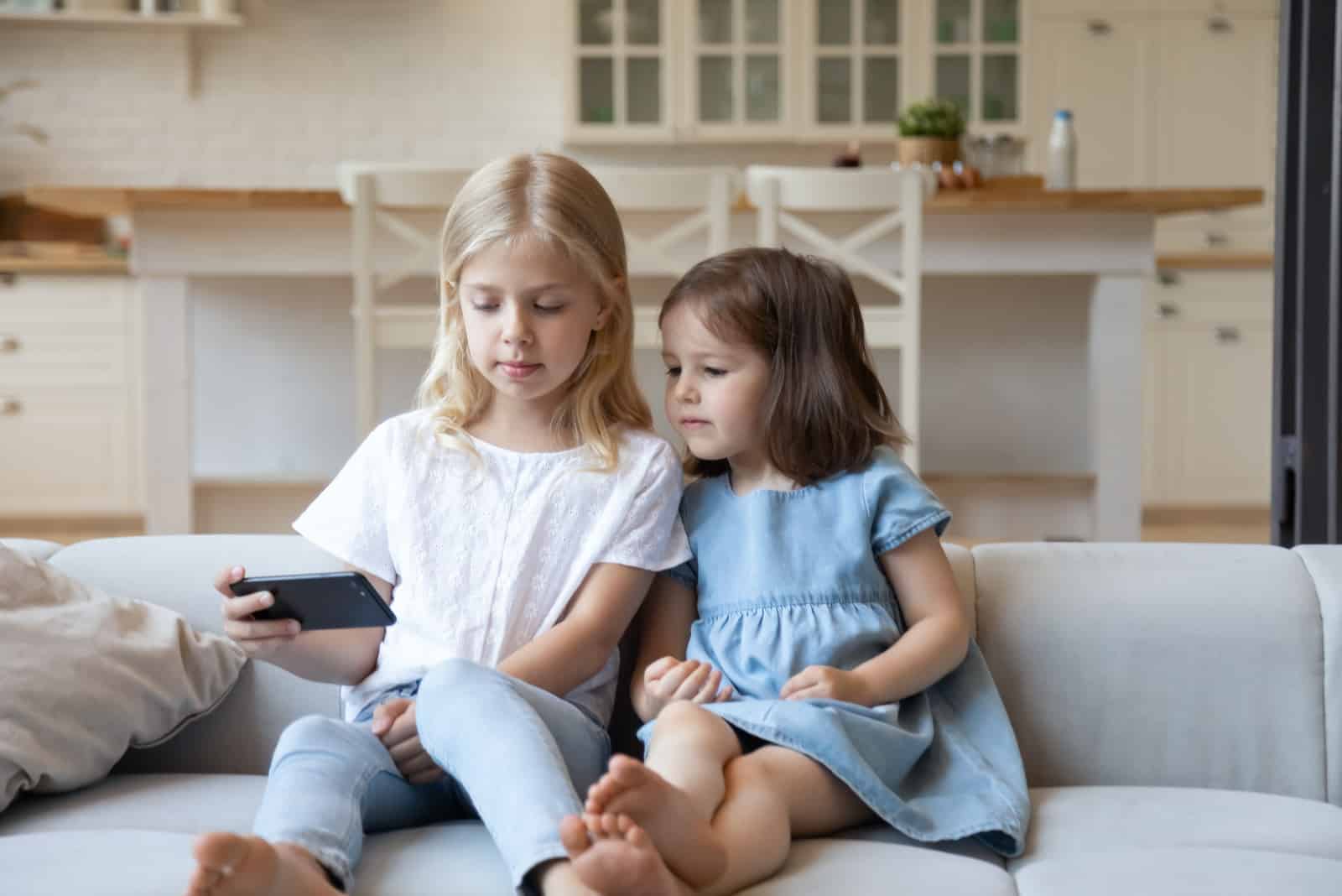 deux petites filles assises sur un canapé regardant le téléphone
