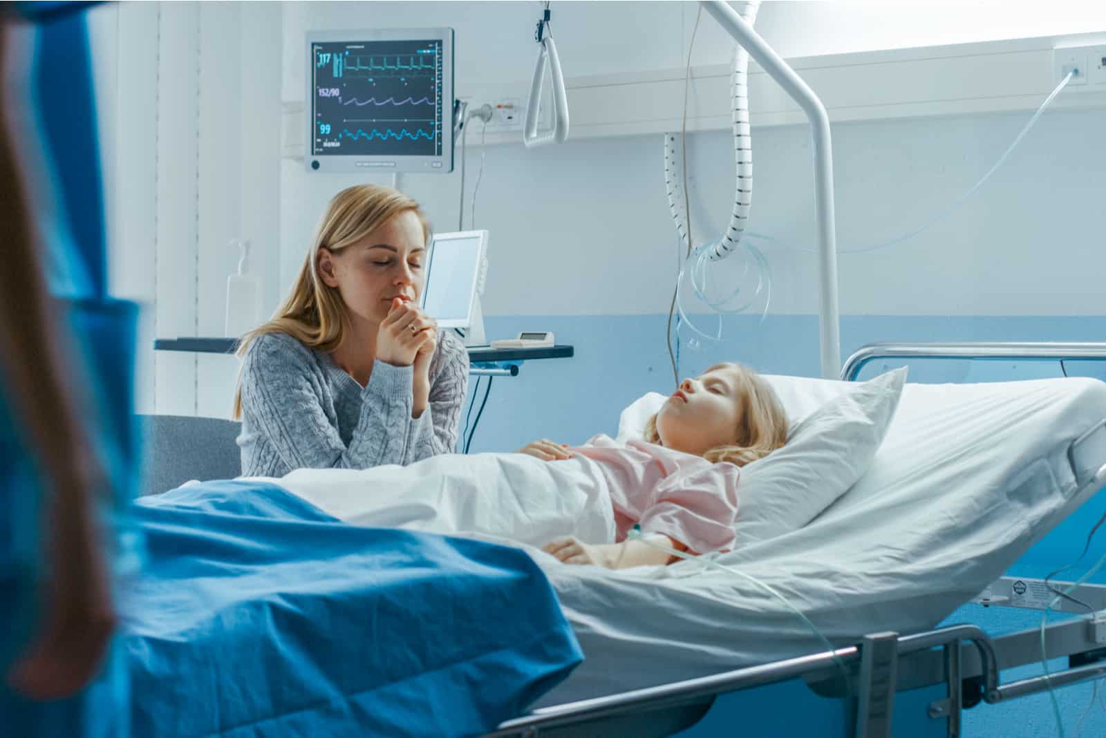 la femme est assise à côté du lit d'un enfant allongé à l'hôpital