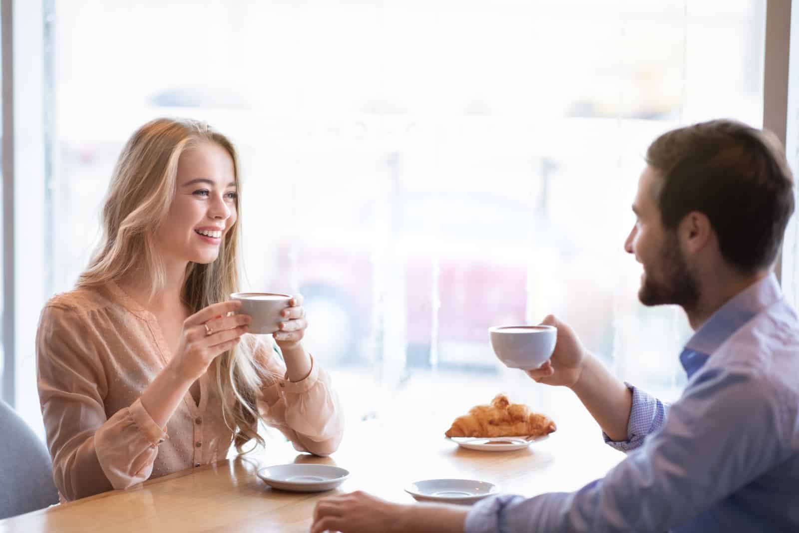 un homme et une femme assis à une table prenant un café en train de parler