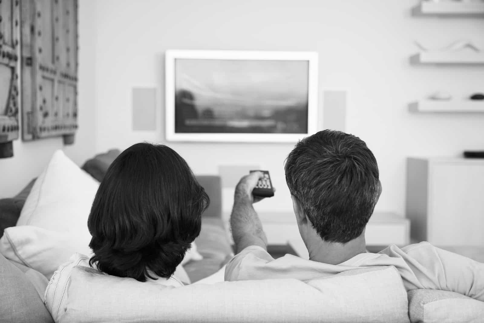un homme et une femme sont assis sur le canapé en train de regarder la télévision