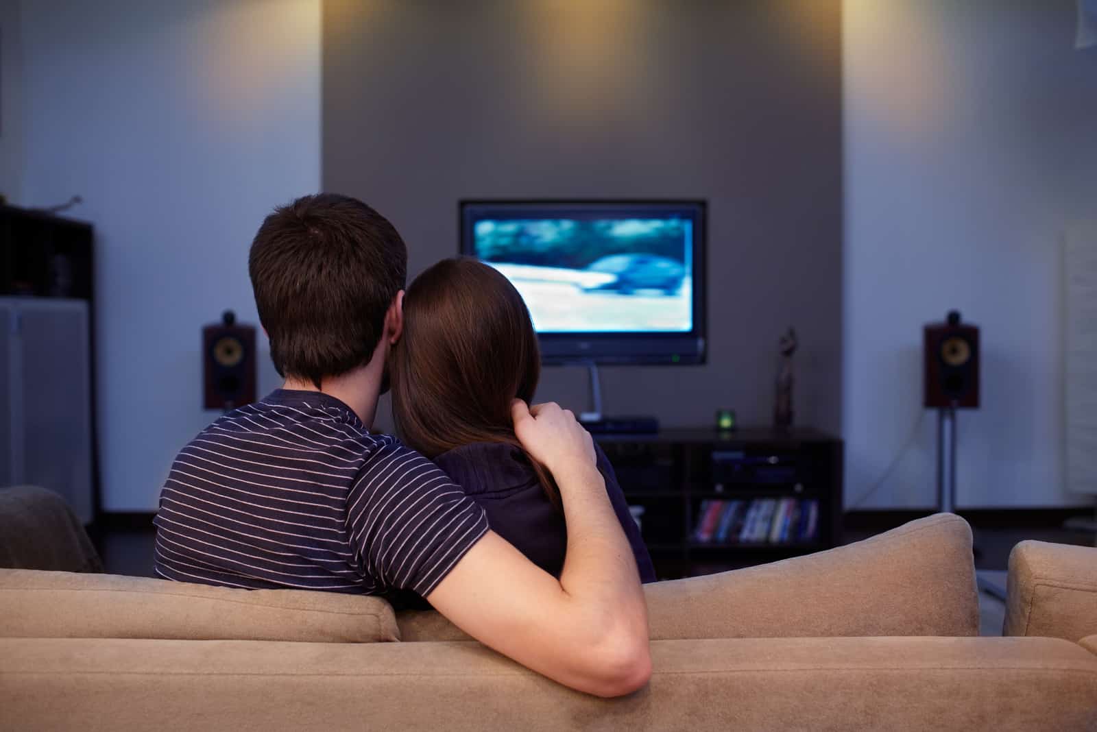 un homme étreignant une femme assise sur le canapé et regardant la télévision