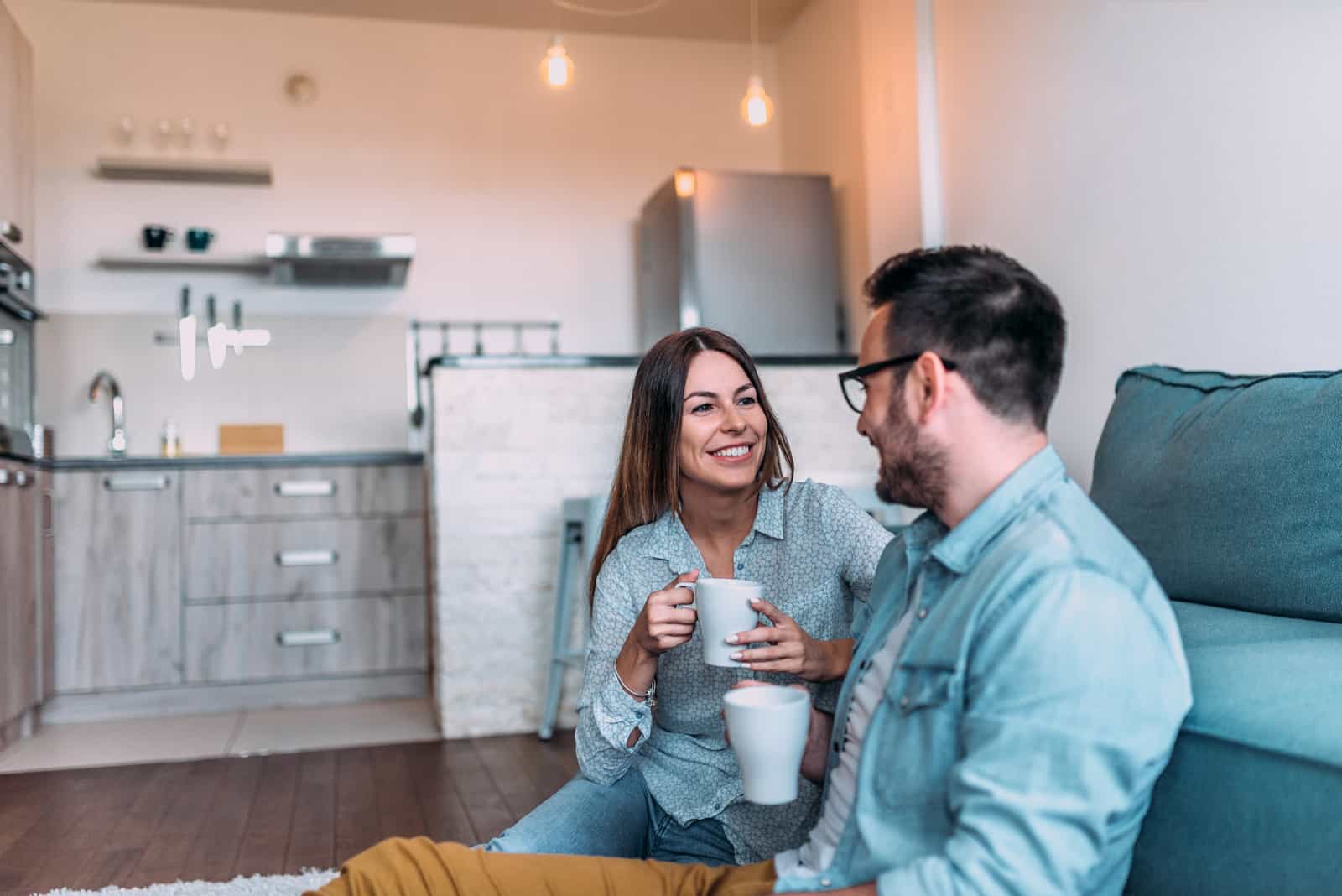 un homme souriant et une femme assise sur le sol prenant un café en train de parler