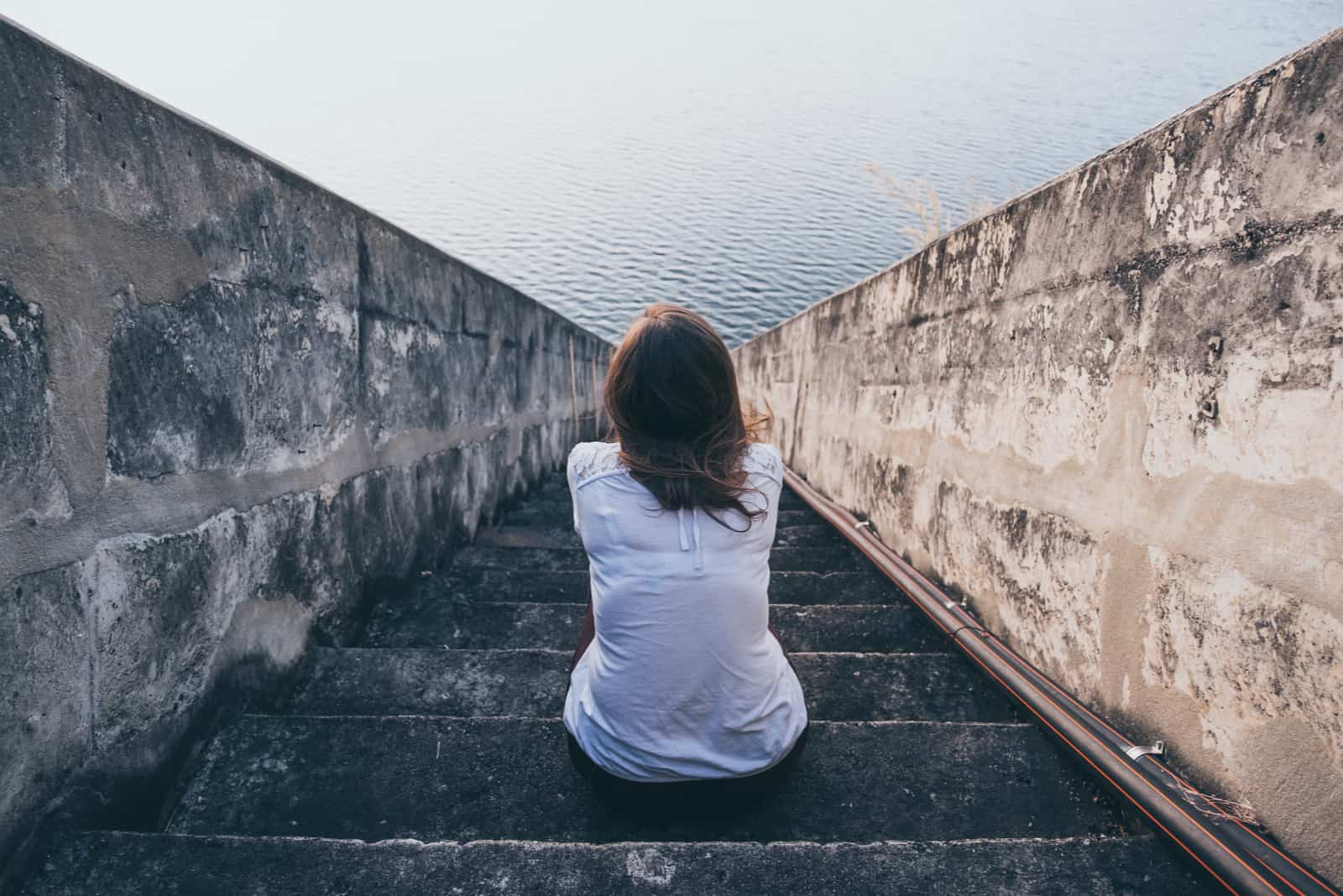 une femme est assise dans les escaliers et regarde la mer