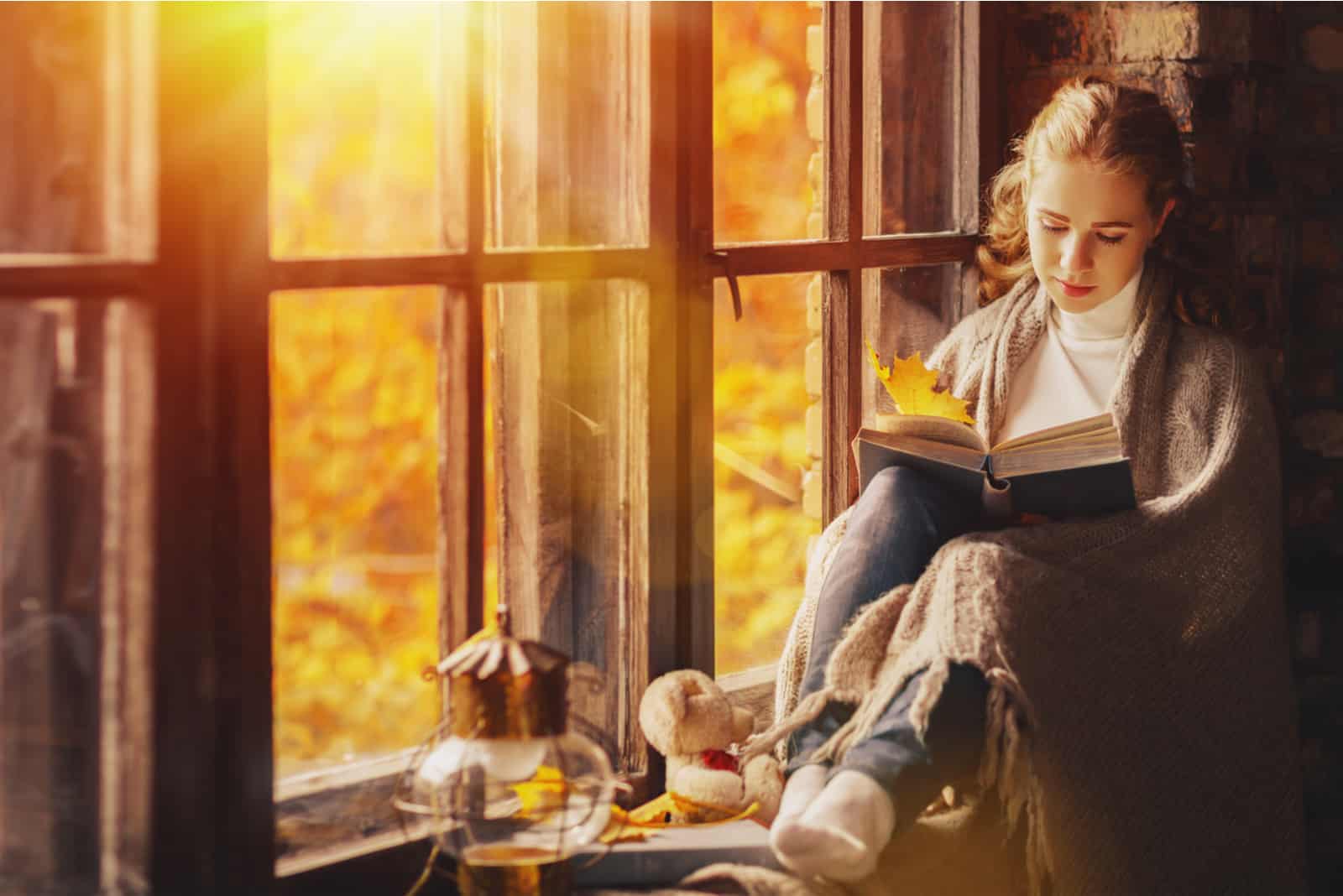 une femme est assise près de la fenêtre et lit un livre