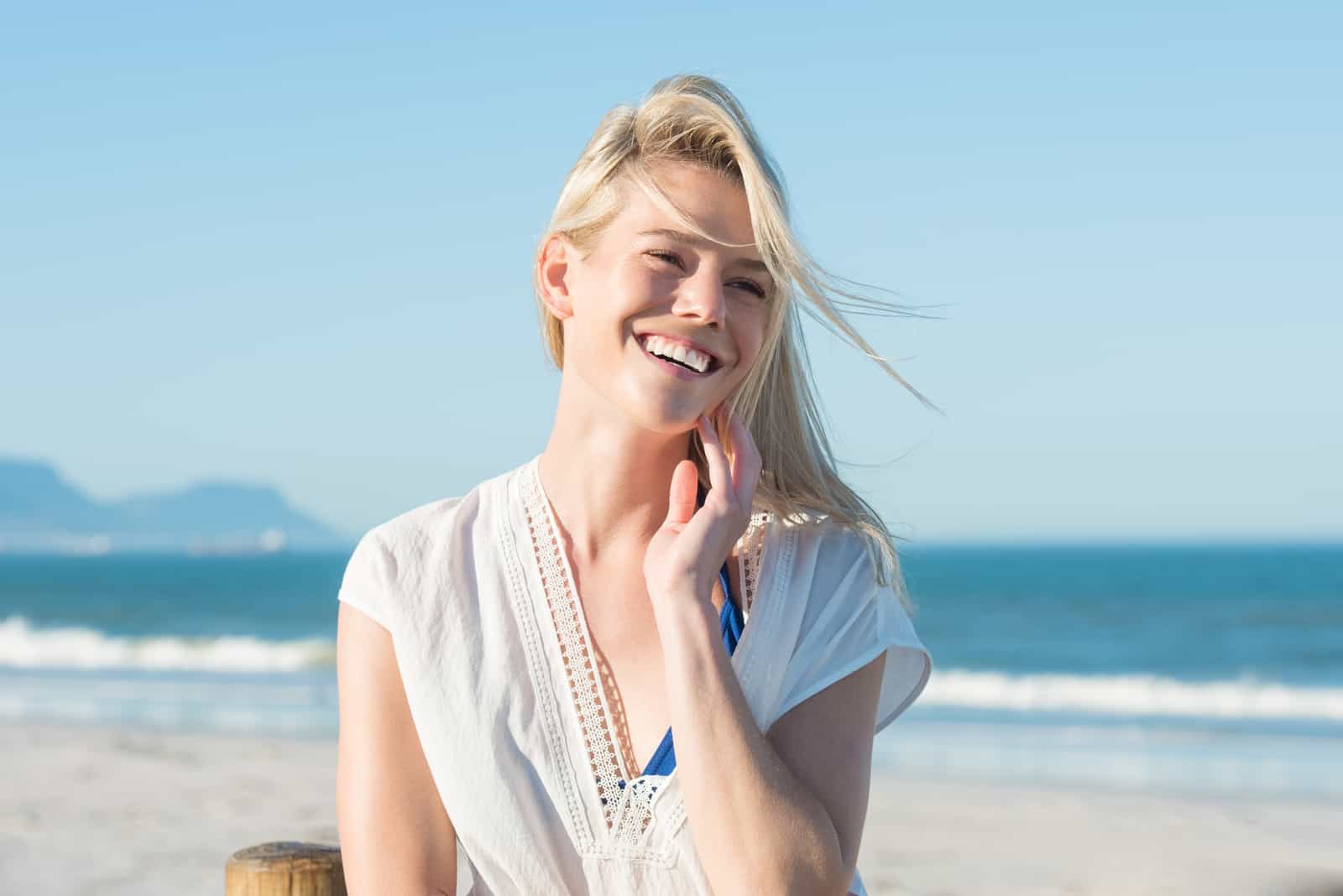 une femme souriante aux longs cheveux blonds est assise sur la plage