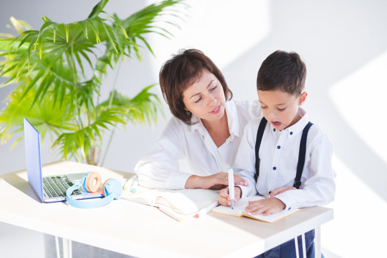 la femme est assise à côté de l'enfant pendant qu'il fait ses devoirs