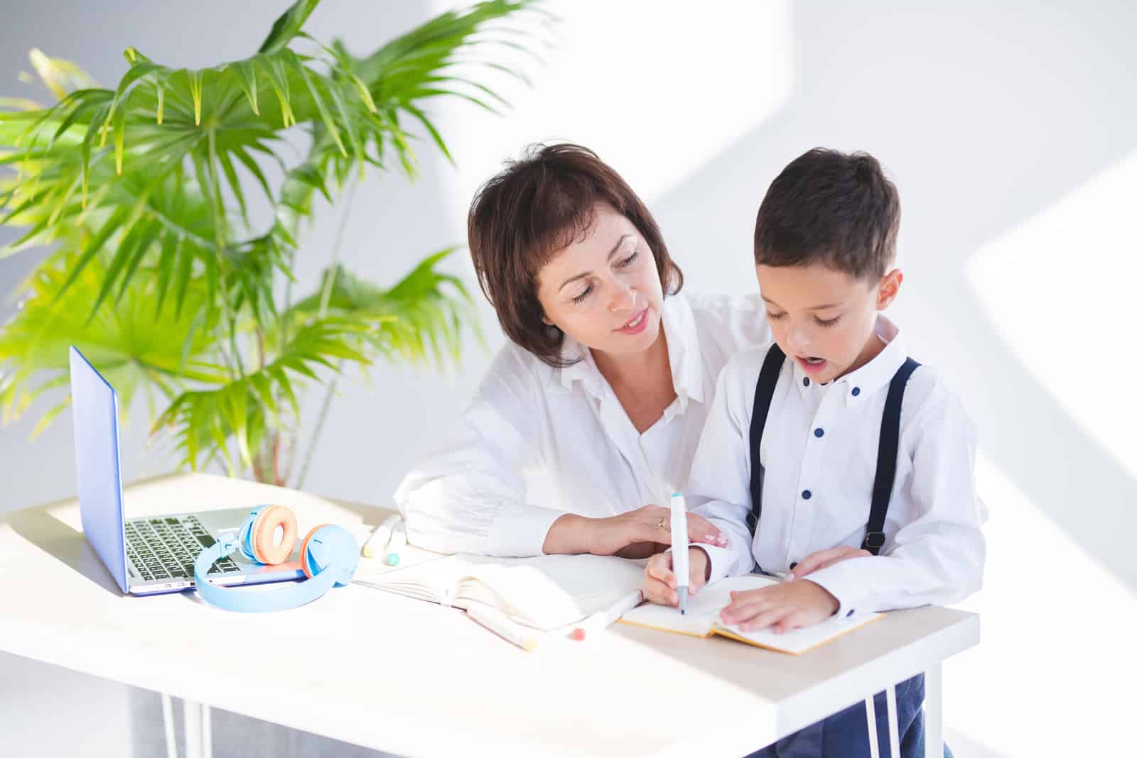 la femme est assise à côté de l'enfant pendant qu'il fait ses devoirs