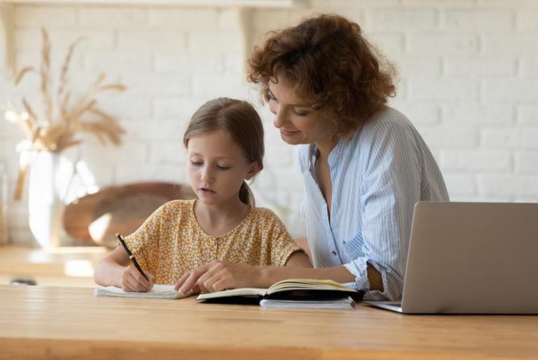 la femme est assise avec la fille à table pendant qu'elle écrit