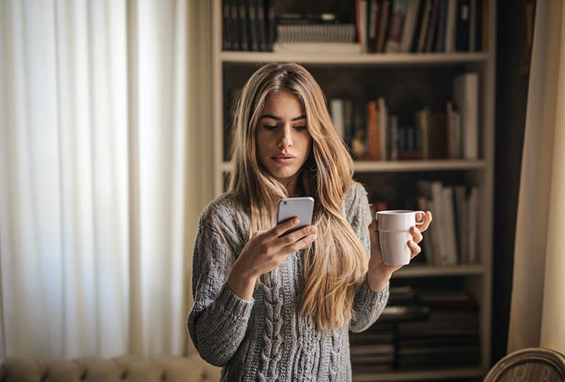 femme pensive utilisant son smartphone et tenant une tasse de café