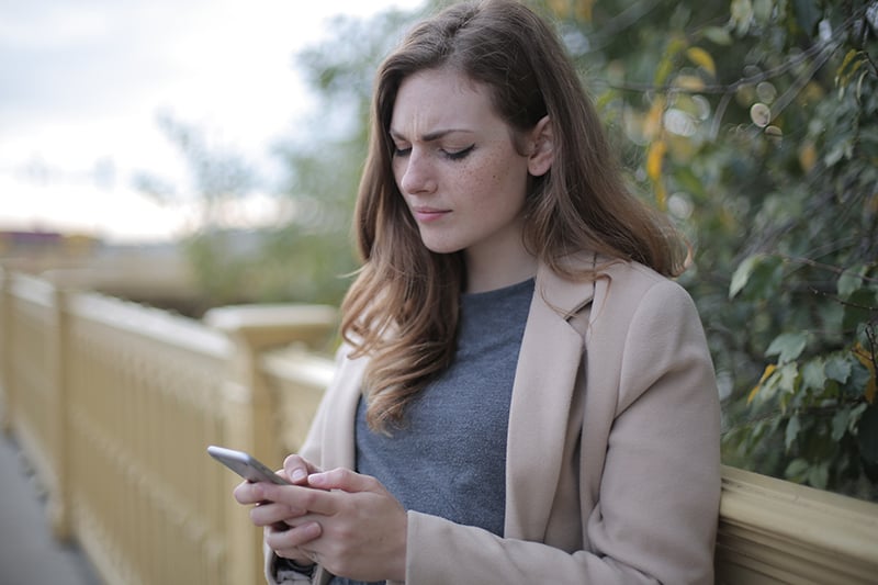 femme pensive utilisant son smartphone en se tenant debout à l'extérieur