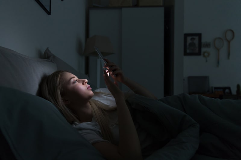 femme utilisant un téléphone dans le lit dans le noir