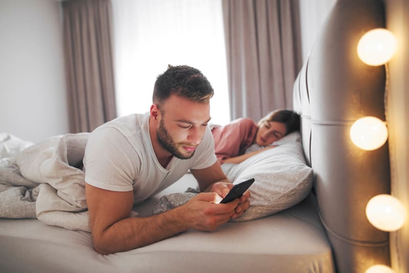 Homme écrivant un message sur un smartphone à côté de sa petite amie endormie