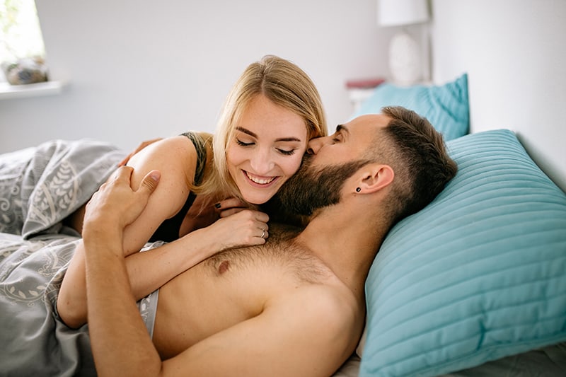 homme embrassant une femme souriante dans le lit