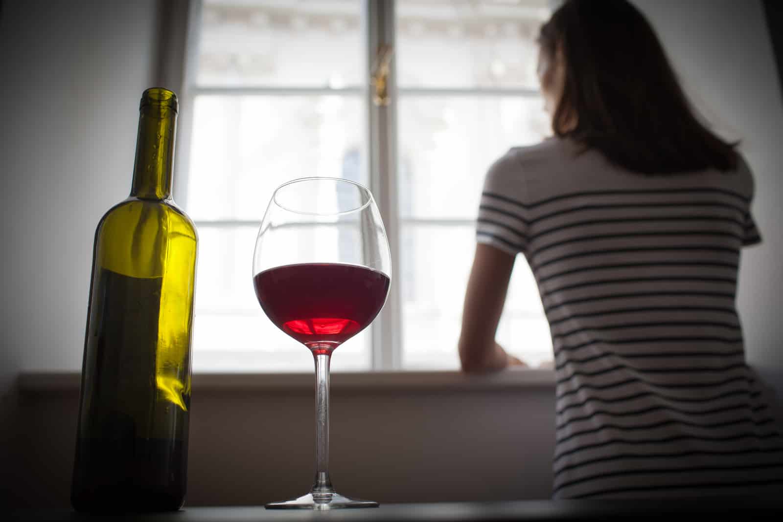sur la table se trouve une bouteille de vin et un verre de femme debout près de la fenêtre