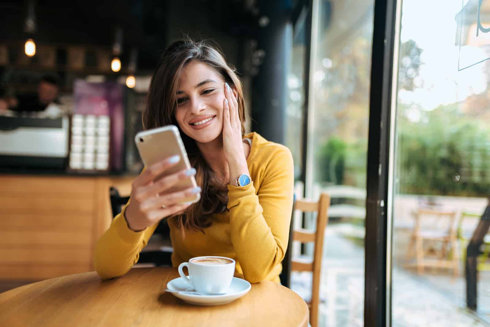 une belle fille est assise dans un café tenant un téléphone à la main