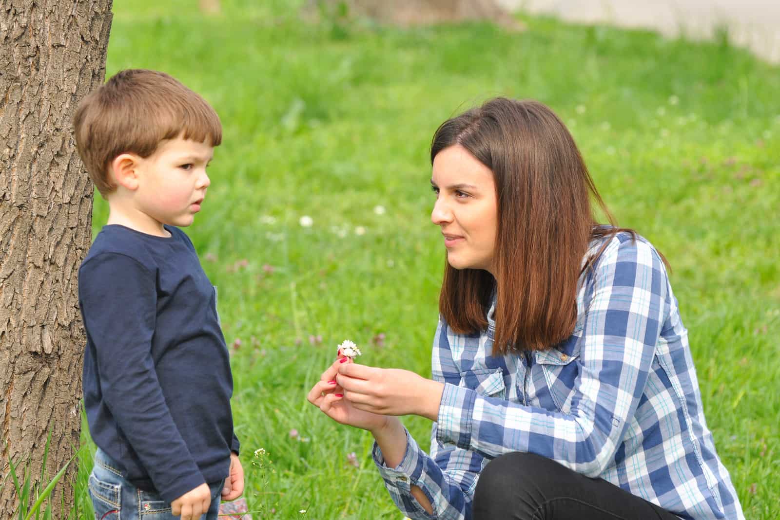 une femme dans le parc montre des fleurs à un enfant pendant qu'il regarde ailleurs