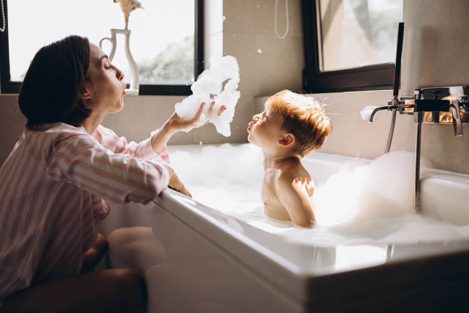 une femme jouant avec un enfant se baignant dans une baignoire