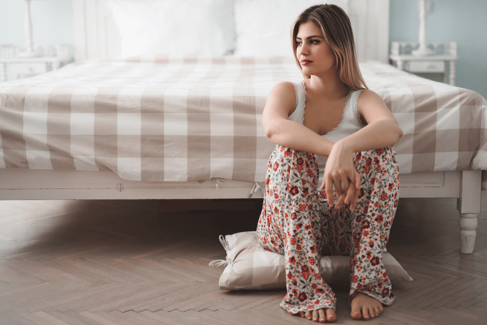 une femme triste est assise sur le sol appuyée contre le lit
