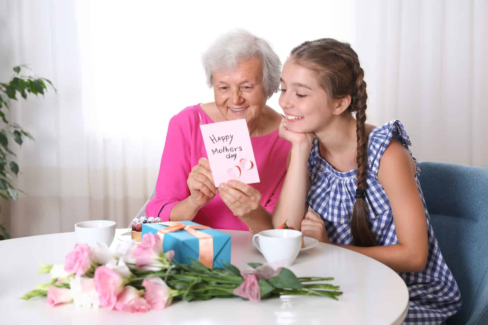 une grand-mère et une petite-fille souriantes s'assoient à une table et lisent une carte de voeux