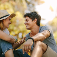 une femme souriante avec un chapeau sur la tête est assise sur l'herbe et parle à un homme