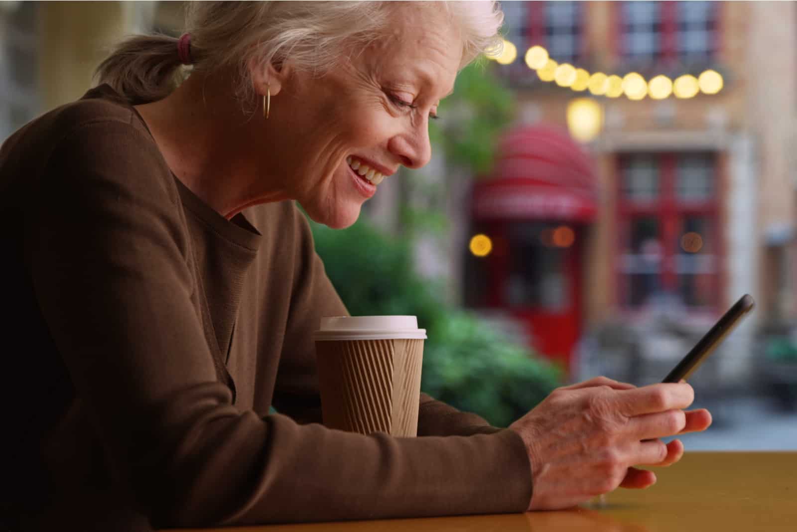 Femme plus âgée assise au café en train de boire du café et d'envoyer des SMS