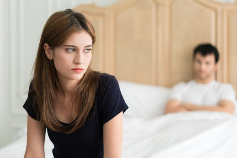 une femme triste est assise sur le lit tandis qu'un homme désintéressé se couche