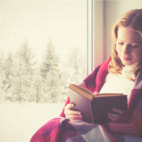 une belle femme est assise près de la fenêtre en lisant un livre