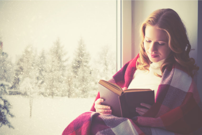 une belle femme est assise près de la fenêtre en lisant un livre