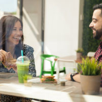 souriant couple d'amoureux assis à l'extérieur prenant un café en train de parler