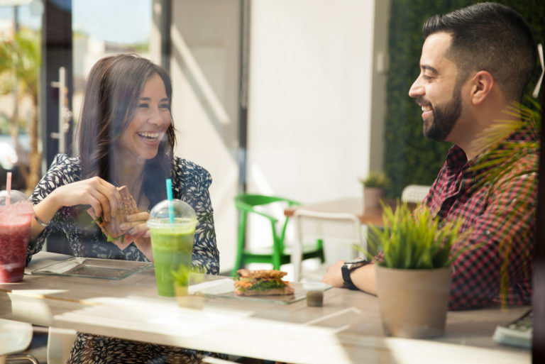 souriant couple d'amoureux assis à l'extérieur prenant un café en train de parler