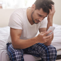 un homme triste assis sur le lit tenant un téléphone à la main