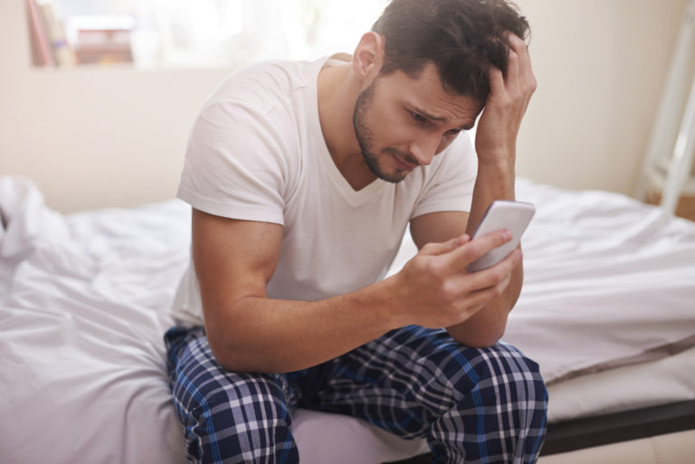 un homme triste assis sur le lit tenant un téléphone à la main