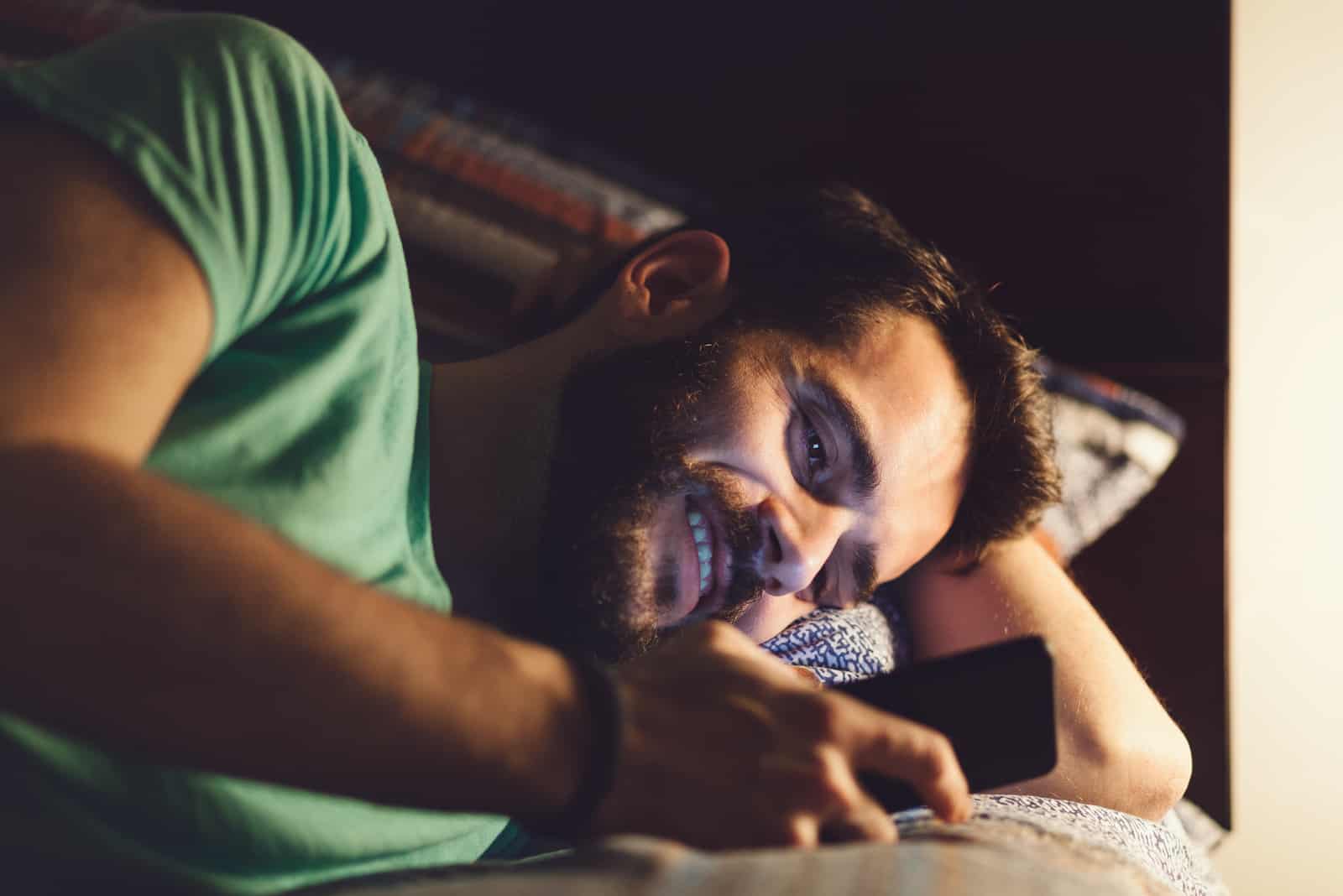 homme heureux allongé dans son lit en train de lire des messages