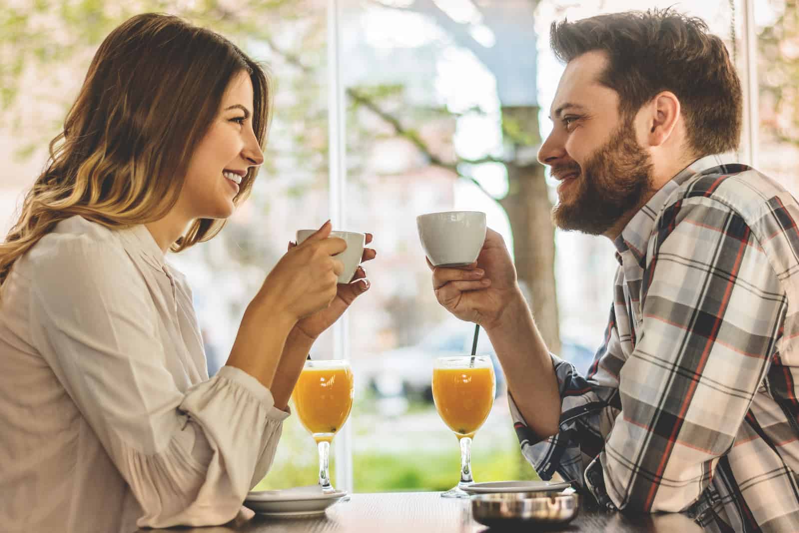 souriant couple d'amoureux assis à l'extérieur prenant un café en train de parler