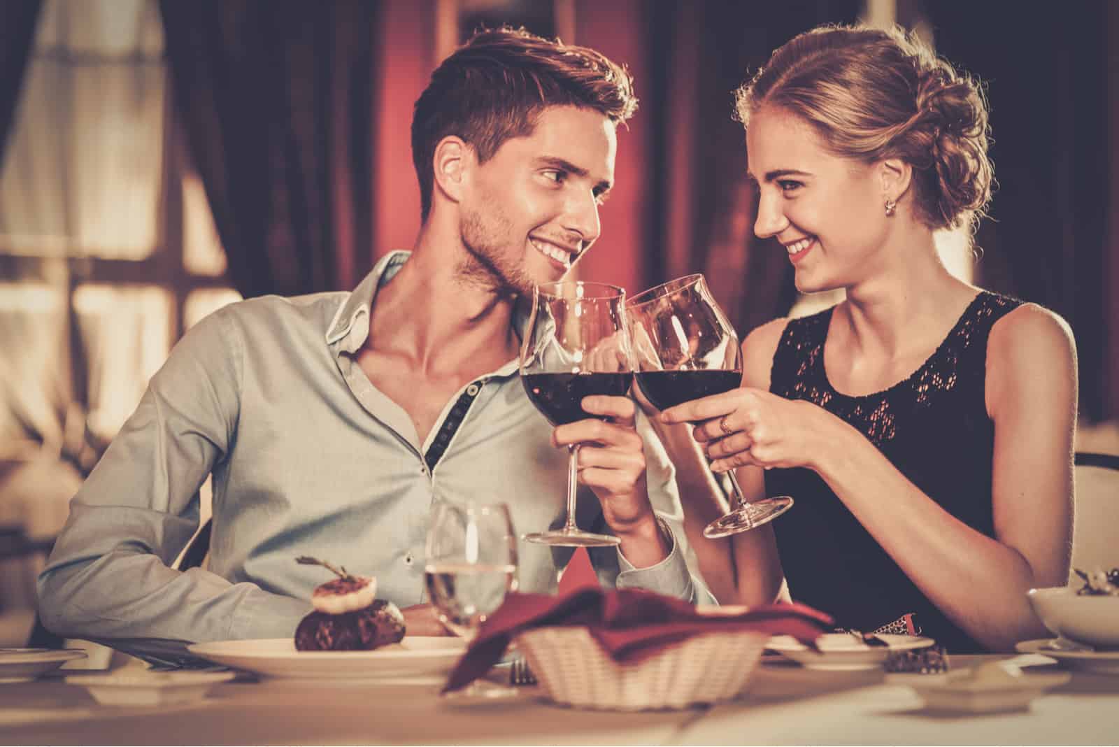 un homme et une femme souriants sont assis à une table et portent un toast avec du vin