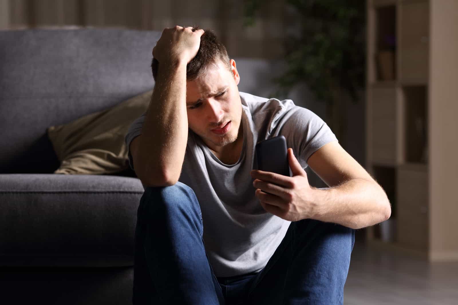 un homme triste assis sur le sol tenant un téléphone à la main