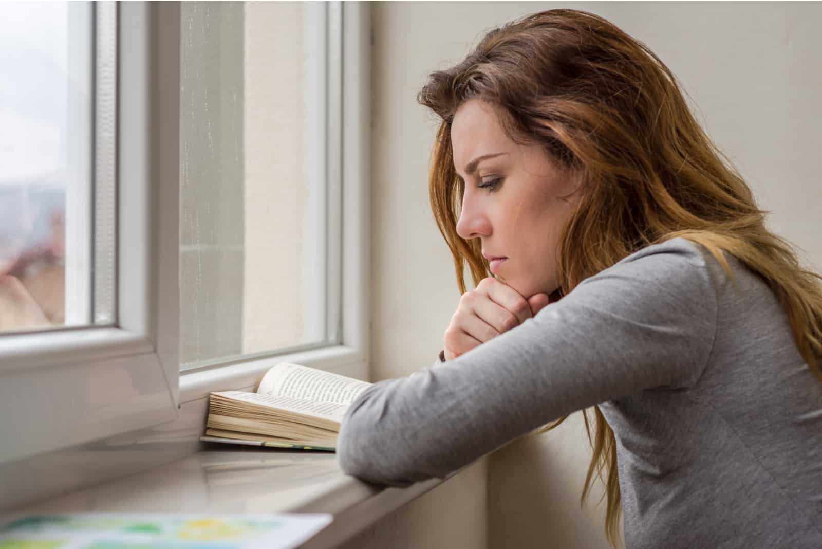 une femme assise près de la fenêtre en train de lire un livre