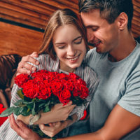 un homme et une femme dans une étreinte alors qu'elle tient un bouquet de roses