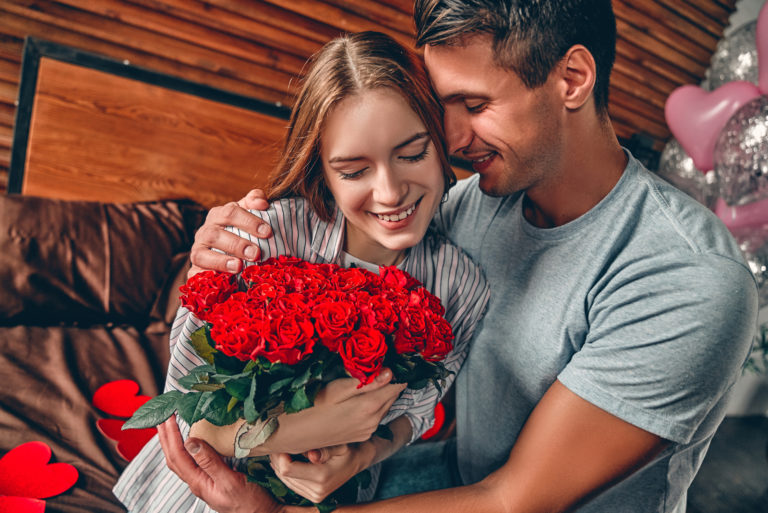 un homme et une femme dans une étreinte alors qu'elle tient un bouquet de roses
