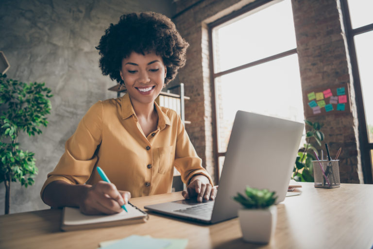 jeune femme souriante écrivant une carte près du bureau avec un ordinateur portable