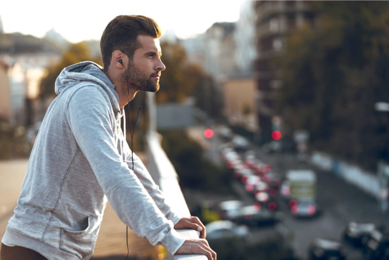 un homme imaginaire avec des écouteurs dans les oreilles se tient appuyé contre une clôture et regarde au loin